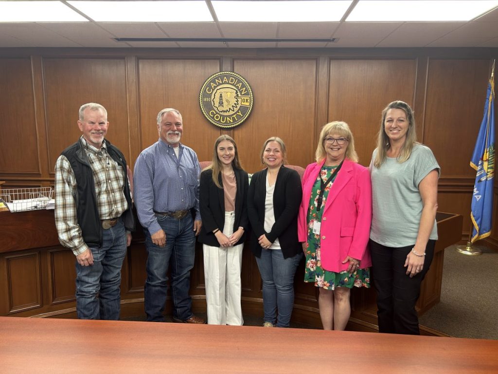 Kailyn Twyman poses with Canadian County Commissioners Tomas Manske, Tracey Rider and Lacey Dawson, along with county staff at the Commissioners meeting April 28. (Photo by Jacob Sturm)